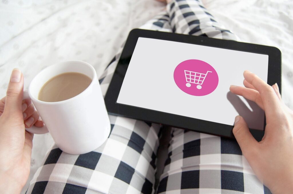 Woman sitting cross-legged with coffee, browsing a shopping cart icon on a tablet