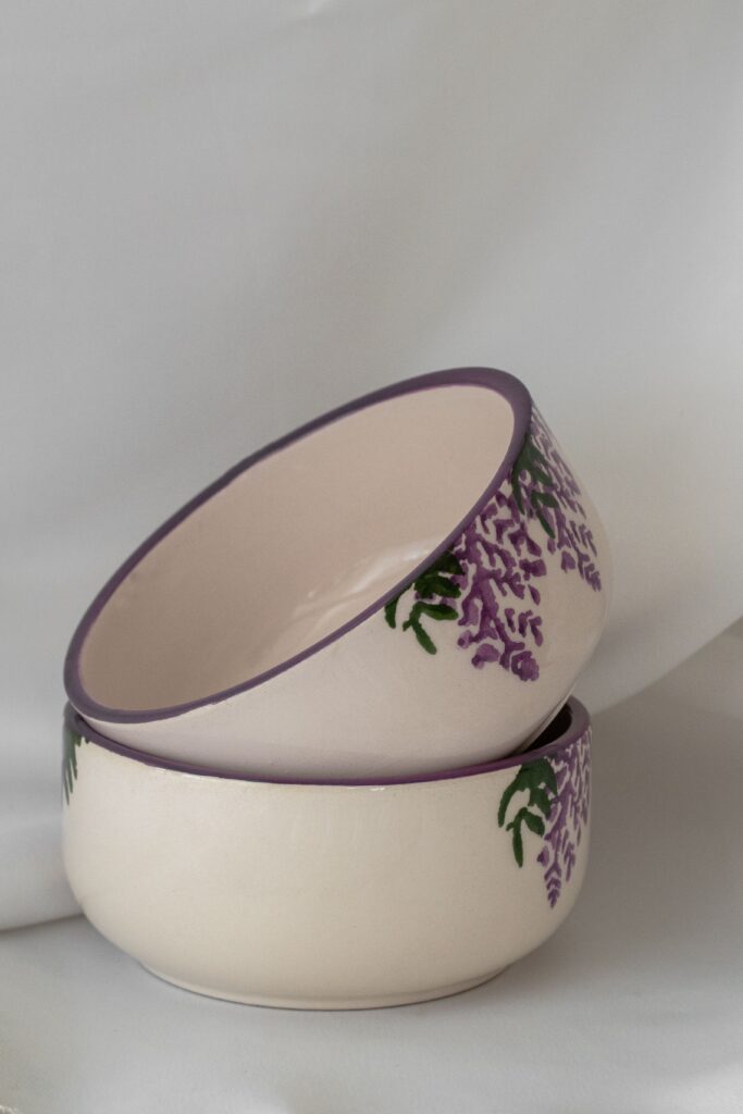 Two cream ceramic bowls with purple floral details stacked together while getting older
