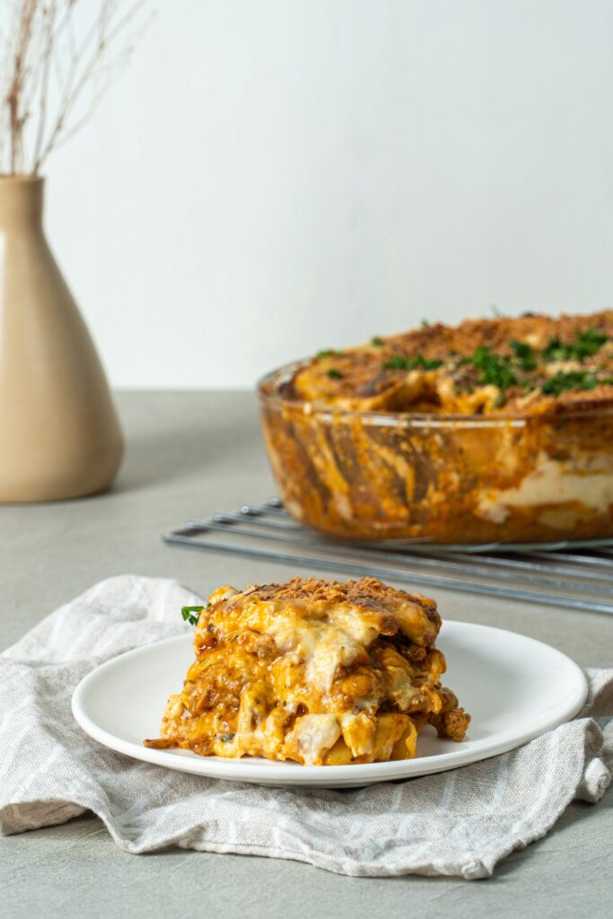 Baked cheesy pasta casserole with a serving plated in the foreground